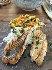 Deliciously prepared fish fillets served on a plate with rice and a colorful mango salad, showcasing a fresh catch from a recent fishing trip.