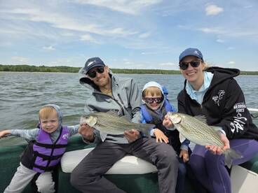A family enjoying a successful fishing trip, proudly displaying their catch of striped bass while out on the water.