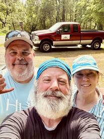 Three anglers posing for a selfie near a truck, likely after a fishing trip, with no visible catch.