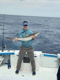 Angler proudly displaying a large shark caught while deep-sea fishing, showcasing the excitement of offshore fishing adventures.