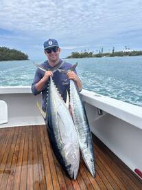 Angler proudly displaying two large Wahoo caught during a fishing trip, with a scenic backdrop of the coastline.