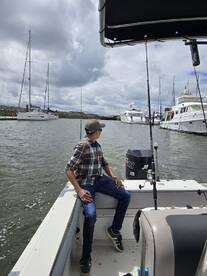 A young man relaxing on the boat, enjoying the scenic view of the marina with multiple yachts in the background.