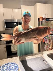 A proud angler displaying a large Red Grouper in a kitchen setting, showcasing a successful fishing trip.