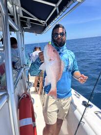 Angler proudly displaying a large Snapper while fishing on a charter boat in clear blue waters.