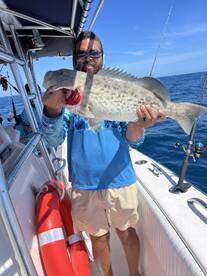Angler proudly displaying a large Grouper while fishing on a charter boat in clear blue waters.