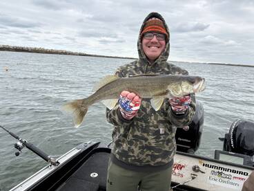 Angler proudly displaying a Walleye while fishing from a boat in a scenic waterway.