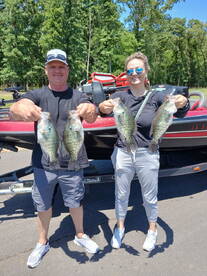 Two anglers proudly displaying their catch of Crappie in front of a fishing boat after a successful day on the water.