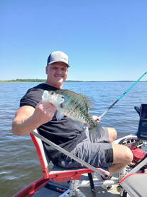 Angler proudly displaying a large Crappie while fishing on a sunny day in a serene lake setting.