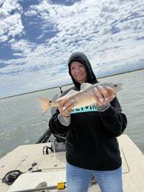 Angler proudly displaying a Redfish while fishing on a boat in a scenic coastal environment.
