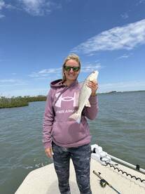 Angler proudly displaying a large Speckled Trout while fishing on a boat in a coastal waterway.