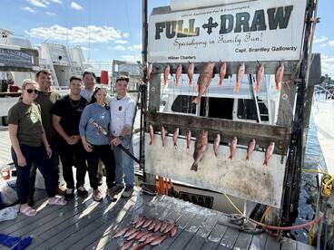 A group of six anglers proudly posing in front of a catch board displaying an array of Snapper after a successful fishing trip.