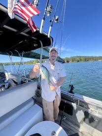 Angler proudly displaying a large Crappie while fishing on a boat, with a scenic backdrop of a bridge and clear blue skies.