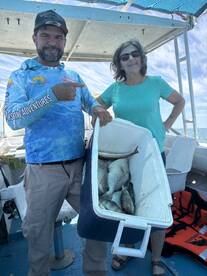Two anglers aboard a boat displaying a cooler filled with various fish after a successful fishing trip.