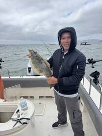 Angler proudly displaying a Flounder caught while fishing from a boat in a coastal area.