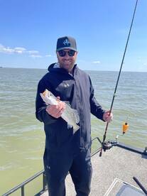 Angler proudly displaying a Speckled Trout while fishing from a boat on a sunny day.