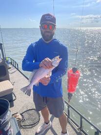 Angler proudly displaying a Speckled Trout while fishing from a boat in a sunny coastal environment.