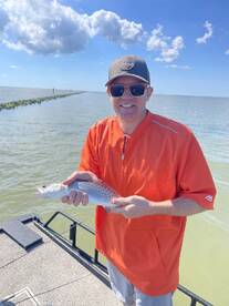 Angler proudly displaying a Speckled Trout while fishing from a boat in a coastal waterway.