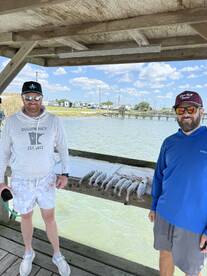 Two anglers proudly posing by a catch of speckled trout displayed on a cleaning table at a dock.