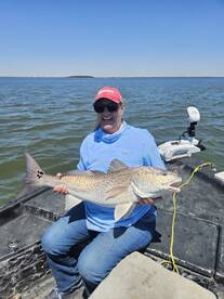 Angler proudly displaying a large Redfish while sitting in a boat on a sunny day.