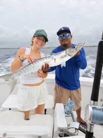 Two anglers proudly displaying a large Barracuda while on a fishing charter, showcasing a successful day on the water.