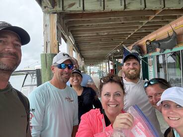 A group of anglers smiling for a selfie at the dock, with a boat in the background and a casual fishing atmosphere.