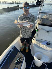 Angler proudly displaying a Speckled Trout while fishing from a boat in calm waters.