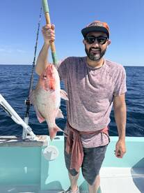 Angler proudly displaying a large Red Snapper while fishing offshore, showcasing a successful day on the water.