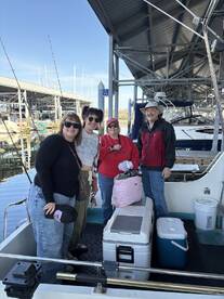 A cheerful group of four adults poses on a boat at the marina, ready for a fishing adventure.