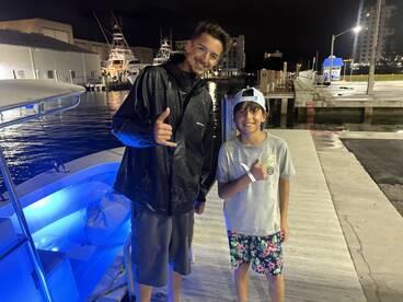 Two individuals posing at the dock near a boat at night, showcasing a fun fishing experience.