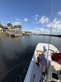 A young angler casting a line from a boat in a scenic waterway, surrounded by palm trees and docks.