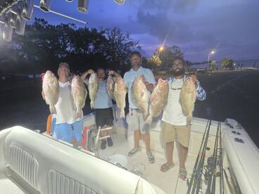 Group of anglers proudly displaying their catch of large grouper on a boat after a successful night fishing trip.