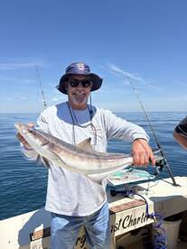 A proud angler displaying a large Cobia while fishing on a charter boat in clear blue waters.