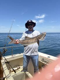 Angler proudly displaying a large shark while fishing on a boat in open water.