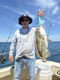 An angler proudly displaying a large Grouper while fishing offshore, showcasing a successful day on the water.