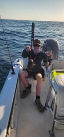 A young angler proudly displaying two caught fish while fishing on a boat, showcasing a successful day on the water.