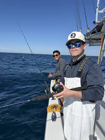 Two anglers actively fishing on a boat, with one reeling in a line while the other enjoys the day on the water.