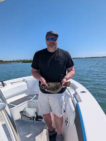 Angler proudly displaying a Flounder on a boat during a fishing trip.