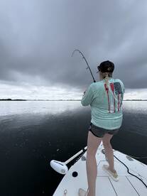 A female angler casting her line from the bow of a boat under overcast skies, showcasing an exciting moment of fishing.