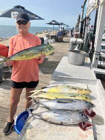A proud angler displaying a large Mahi Mahi alongside several other fish on a dock after a successful fishing trip.