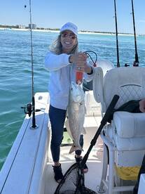 A proud angler holding a large Redfish while fishing on a sunny day, showcasing a successful catch from a boat.