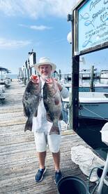 Angler proudly displaying two large Grouper at the dock after a successful fishing trip.