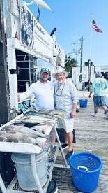 Two anglers proudly displaying their catch of various fish, including Mahi Mahi, at a dockside cleaning station after a successful fishing trip.