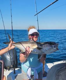 A proud angler holding a large Amberjack while fishing in open waters, showcasing a successful day on the boat.