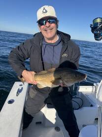 Angler proudly displaying a large Cod while fishing on a boat in open waters.