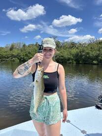 Angler proudly displaying a large Speckled Trout while fishing in a scenic waterway, showcasing a beautiful day on the water.