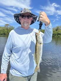 Angler proudly displaying a large Speckled Trout while fishing in a scenic waterway.