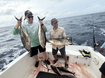 Two anglers proudly displaying their catch of Yellowfin Tuna aboard a fishing boat in open waters.