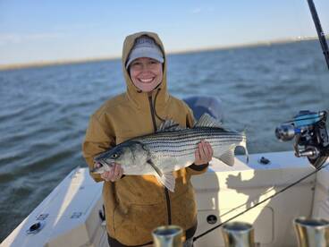 Angler proudly displaying a large Striped Bass while on a fishing trip, showcasing a successful catch in a scenic waterway.