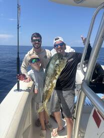 A young angler proudly displays a large Mahi Mahi alongside two adults on a fishing trip in open waters.