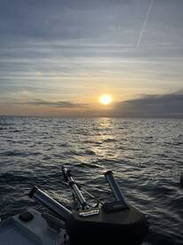 A serene sunset view over the ocean, showcasing the side of a fishing boat with rod holders, perfect for an evening fishing trip.